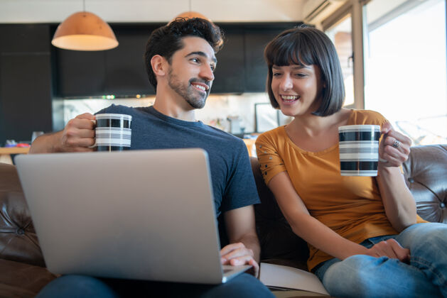 一起一对年轻夫妇坐在家里的沙发上 一起使用笔记本电脑的照片生活房子科技