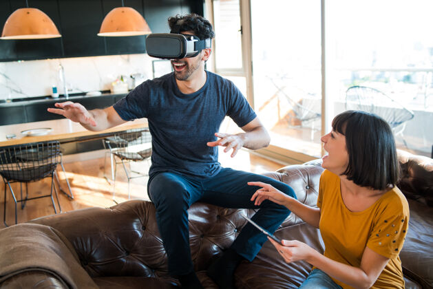 设备一对年轻夫妇在家里玩游戏 戴着虚拟现实眼镜玩游戏游戏耳机模拟