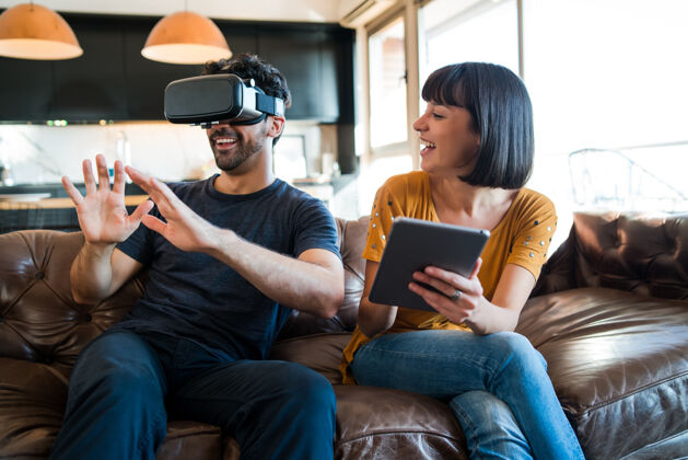 平板电脑一对年轻夫妇在家里玩游戏 戴着虚拟现实眼镜玩游戏年轻人虚拟沙发