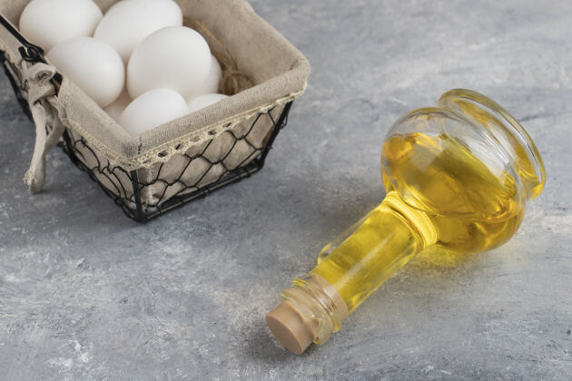 家禽装满新鲜的白色鸡蛋的篮子 大理石上放着一瓶玻璃油食物鸡蛋农产品