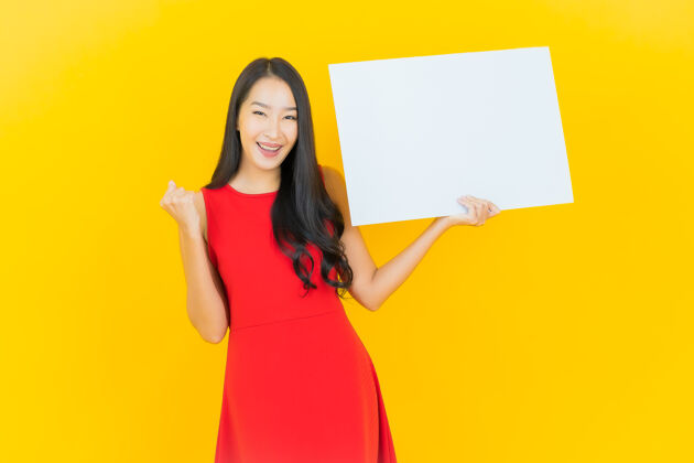 海报一幅美丽的亚洲年轻女子微笑的画像 黄色的墙上挂着白色的广告牌持有空白休闲