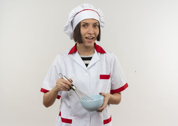 搅拌快乐的年轻女厨师 身着厨师制服 手拿搅拌器和碗 孤立地站在白色地板上快乐厨师年轻