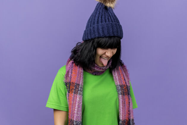 穿愁眉苦脸的年轻病妇戴着冬天的帽子和围巾把头转向一边 在紫色的墙壁上露出孤立的舌头 还有复制空间围巾侧线感情