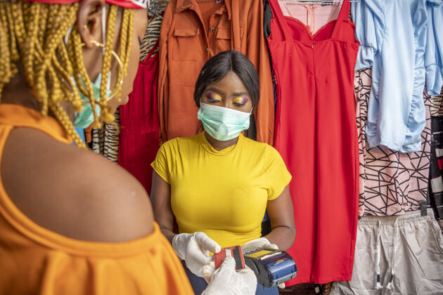 购物者特写镜头：一名非洲女性戴着乳胶手套和口罩 在商店用信用卡付款手套市场病毒