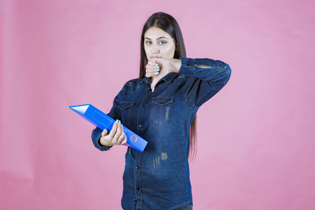 女性女商人拿着一个蓝色文件夹 并显示拇指向下的标志随意人类不成功