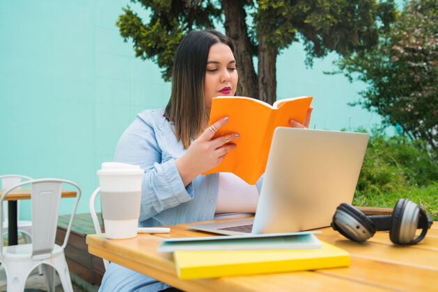 工作年轻女子坐在咖啡馆户外用笔记本电脑和书学习的画像笔记桌子教育