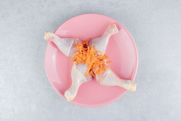 可口把鸡腿和碎胡萝卜放在盘子里 放在大理石表面有机感恩美味