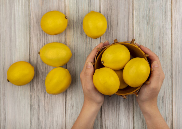 木材女性手拿着一桶健康柠檬的顶视图 柠檬被隔离在灰色的木制背景上块水果切片