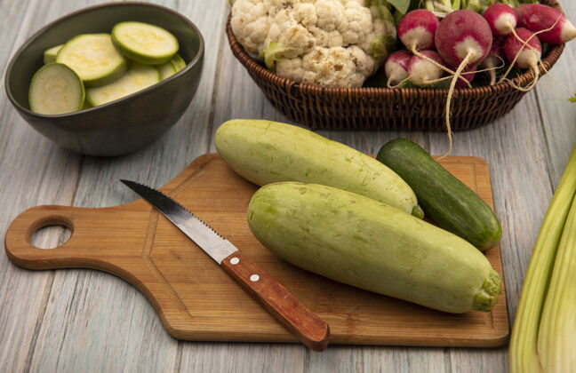 食物健康蔬菜的俯视图 如西葫芦和黄瓜在一个木制的菜板上 在灰色的木制背景上 用刀和切碎的西葫芦放在一个碗上视图黄瓜刀