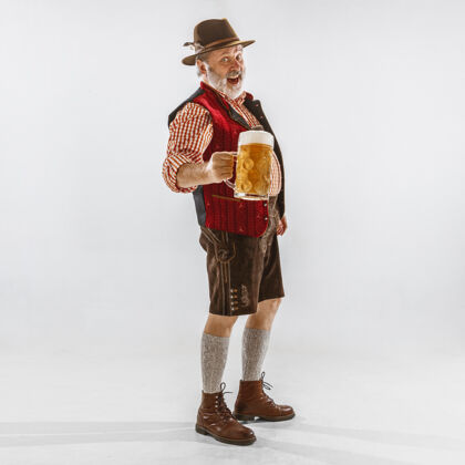 老年人啤酒节高级男士的肖像 戴着帽子 穿着传统的巴伐利亚服装在白色背景的摄影棚拍摄的男性全长庆祝 节日 节日的概念喝啤酒商人巴伐利亚节日