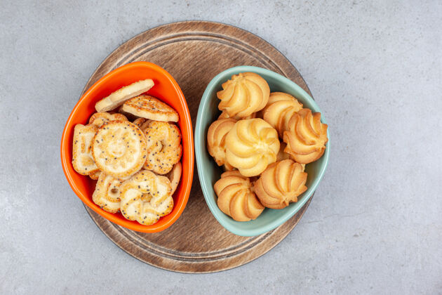 午餐两碗饼干和饼干片放在大理石背景的木板上高质量的照片各色美味薯片
