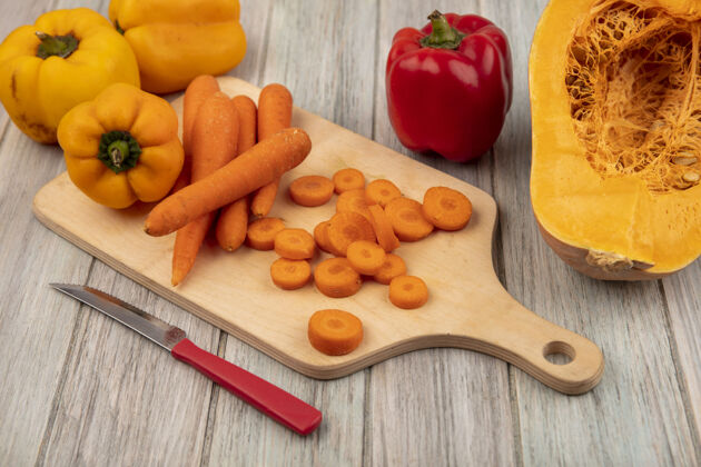 视图木制菜板上橘皮胡萝卜的俯视图 刀子上的彩色甜椒被隔离在灰色的木制背景上食物胡椒刀