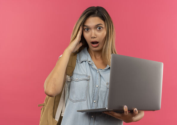 背印象深刻的年轻漂亮的学生女孩穿着背包拿着笔记本电脑把手放在头上孤立的粉红色学生穿印象