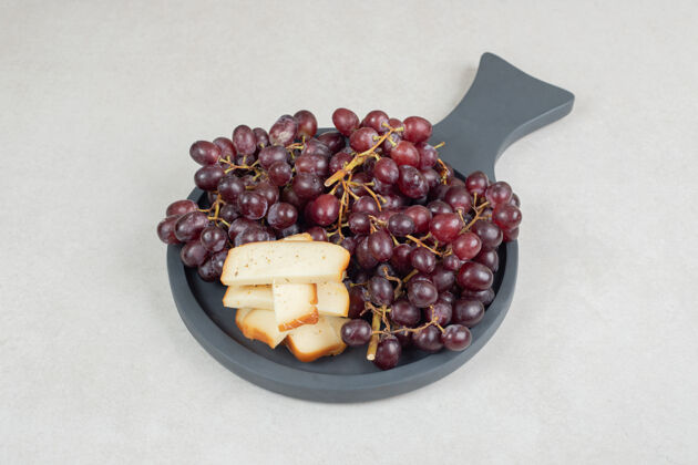 浆果新鲜的红葡萄和奶酪片放在深色的木板上葡萄簇状成熟