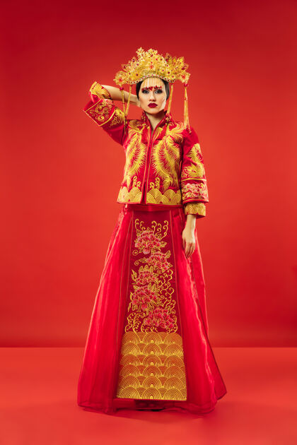 服装中国传统的优雅女子在摄影棚的红色背景美丽的女孩穿着民族服装中国新年 优雅 优雅 表演者 表演 舞蹈 女演员 情感概念微笑女性女孩