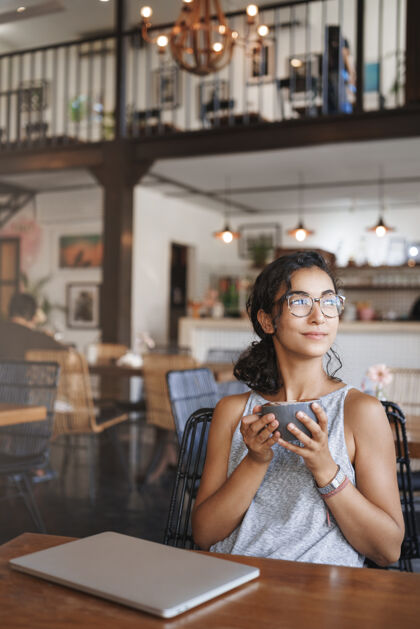 放松垂直拍摄温柔放松的都市女人戴着眼镜享受独自坐在咖啡馆的时刻窗口年轻咖啡馆