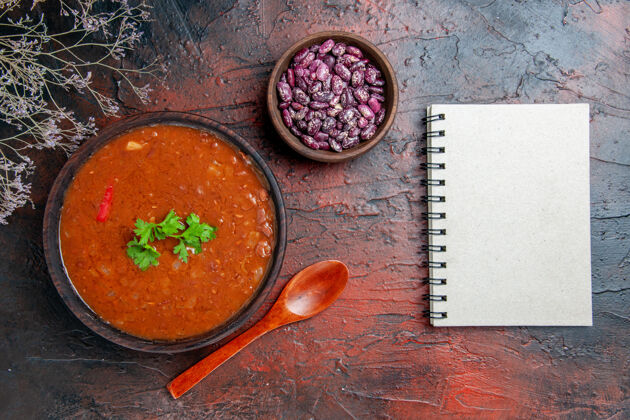 碗经典的西红柿汤在一个棕色的碗豆和汤匙旁边的笔记本上混色表餐厅豆子蔬菜