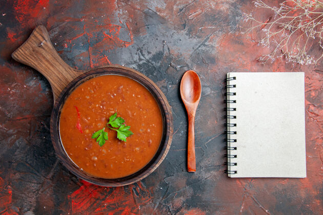 勺子番茄汤放在棕色的砧板上 笔记本放在五颜六色的桌子上餐厅碗容器