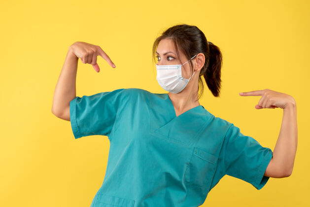 女医生正面图黄色背景上穿着医用衬衫 戴着无菌口罩的女医生指着自己黄色成人人