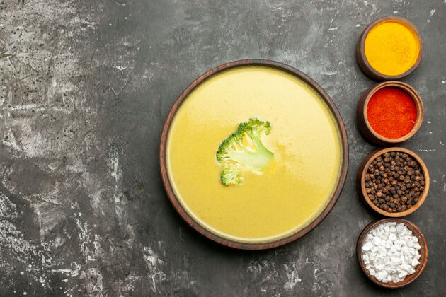 健康棕色碗里的奶油西兰花汤和灰色桌子左侧的不同香料热的容器蔬菜