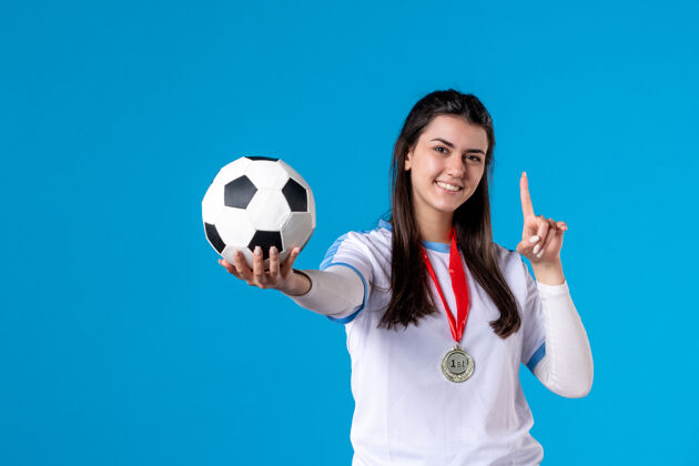 比赛前视图：年轻女子在蓝色墙上拿着足球比赛前面蓝色