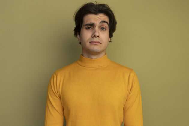 奥利弗自信的年轻帅哥穿着黄色高领毛衣隔离在橄榄绿的墙上高领毛衣男人年轻