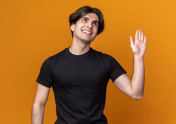 T恤微笑的年轻帅哥穿着黑色t恤 在橙色的墙上显示问候的手势你好手势微笑