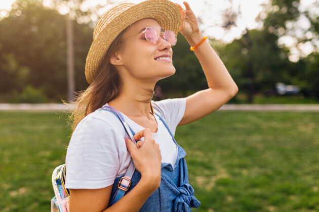时尚戴着草帽 戴着粉色太阳镜 微笑着行走在公园里的年轻漂亮女人的肖像 夏日时尚的风格 五颜六色的时髦装扮酷太阳镜阳光