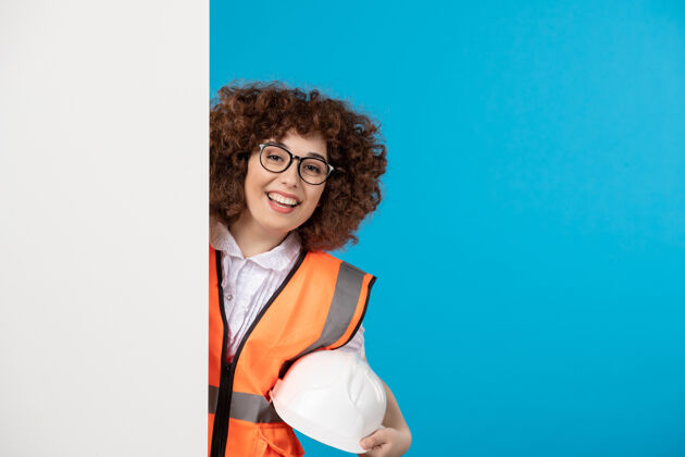 人女建筑工人在统一的蓝色墙前视图微笑女性肖像