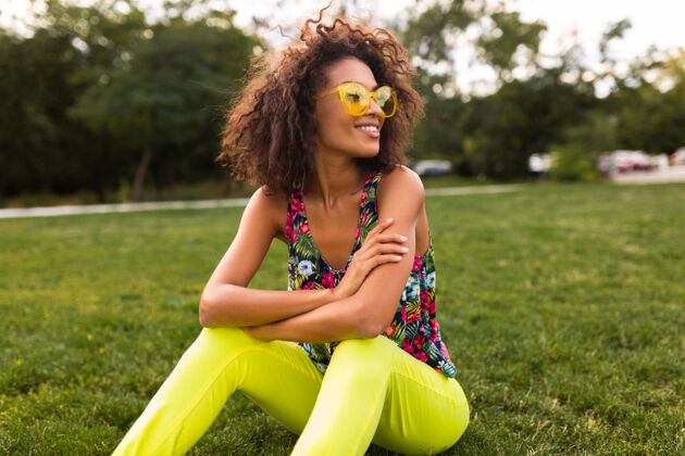 黑色年轻时尚的黑人女子在公园享受夏日时尚的乐趣 五颜六色的时髦装扮 坐在草地上混血儿黄色非洲裔