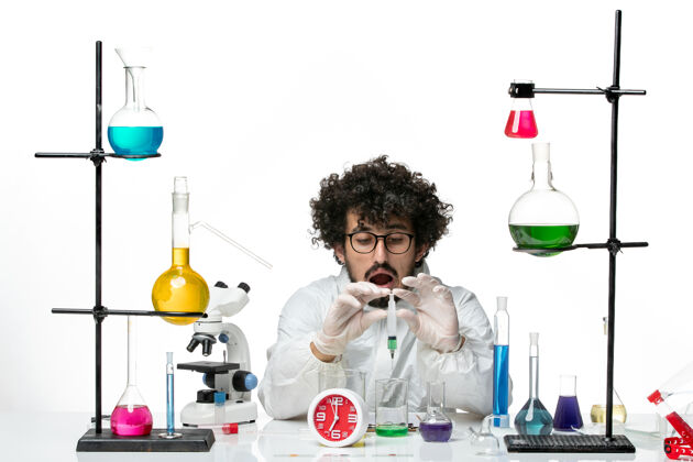 化学正面图身着特殊套装的年轻男性科学家在白墙上注射和溶解溶液套装研究