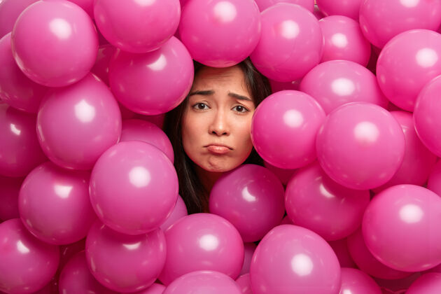 气球心烦意乱的可怜的亚洲女人被粉红色的气球包围 心情不好无聊的生日聚会消极的情绪概念失望发型女士
