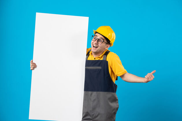 男性身穿黄色制服和头盔的男性建筑工人正视图 蓝色墙上有平面图黄色成人工作