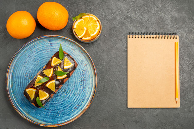 容器黑色桌子上笔记本旁边的软美味蛋糕和橘子的水平视图餐水平食品