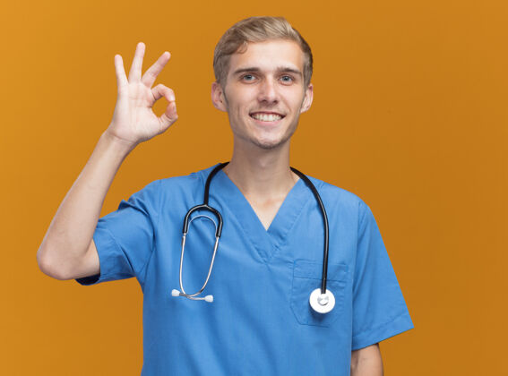 制服微笑的年轻男医生穿着医生制服 听诊器显示出良好的姿态隔离在橙色墙上男性手势展示