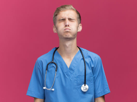 佩戴年轻的男医生穿着医生制服 把听诊器隔离在粉红色的墙上男性医生年轻