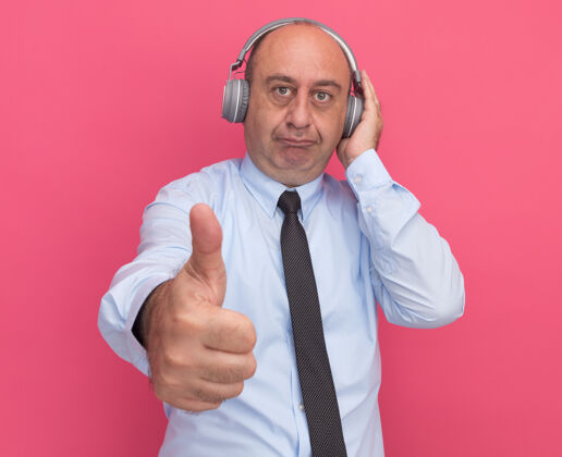 男士一个穿着白色t恤 打着领带 戴着耳机的中年男子在粉红色的墙上孤立地竖起大拇指领带穿中年