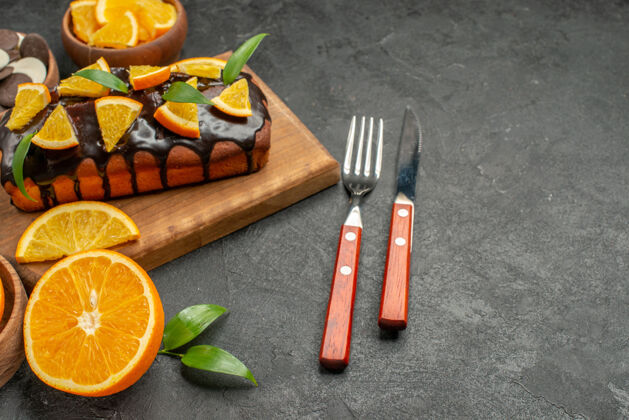 叉子在木制砧板上放软蛋糕 用树叶切橘子 饼干 叉子和刀子柠檬木头晚餐