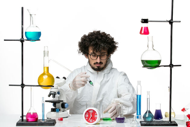 化学正面图身着特殊套装的年轻男性科学家在白桌病毒疫苗注射和溶液上工作-实验室化学科学研究实验室科学