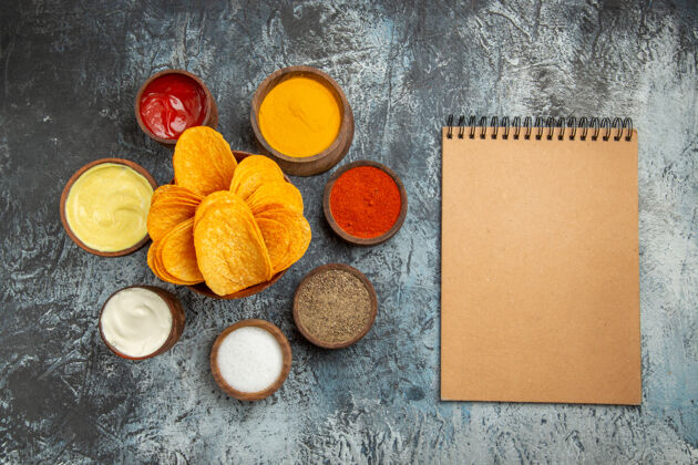 纸板木制砧板上的脆片水平视图 灰色桌子上有不同香料的蛋黄酱番茄酱和笔记本服务纸张香料