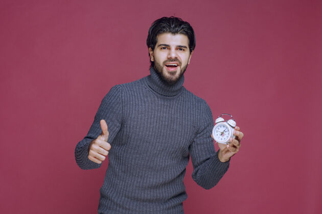 拇指一个男人拿着一个白色闹钟 指着一个最好的报价模特照片工人