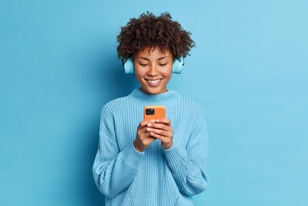 科技笑容可掬的千禧一代美女工作室拍摄用手机上网交流戴立体声耳机选歌听态度请使用