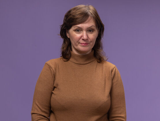 年龄身穿棕色高领毛衣的中年妇女站在紫色的墙上 带着怀疑的表情立场女人高领毛衣