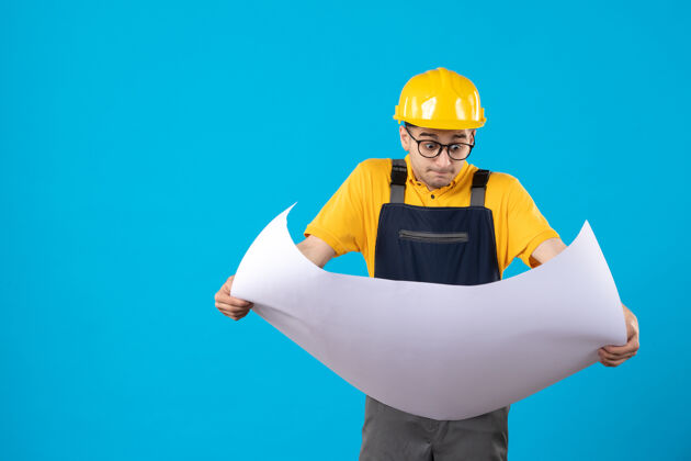 承包商身穿黄色制服的男建筑工人的正视图 蓝色平面图建筑商建筑师工程师
