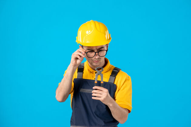 承包商穿着黄色制服的男工人正看着蓝色的钳子制服帽子工作