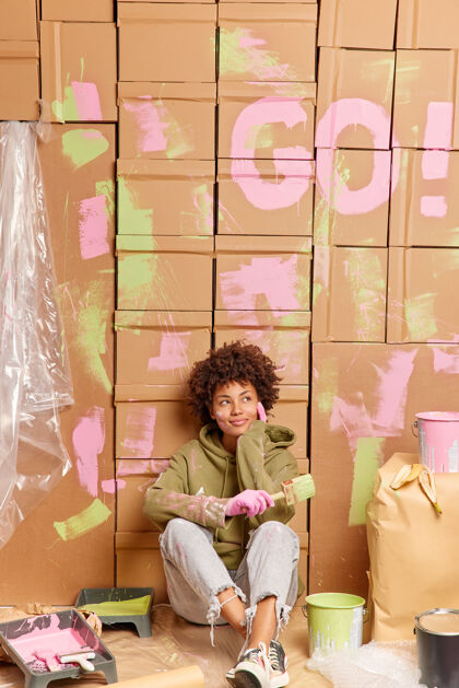 家务体贴的年轻美国黑人妇女坐在地板上休息 装修完新房子 拿着刷子刷墙壁 思考新的室内设计 在新的公寓里 在家里更新后休息滚筒沉思垂直