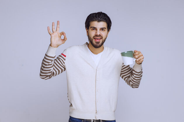 男性一个穿着白衬衫的男人拿着一个咖啡杯 做着一个好手势员工摄影成人