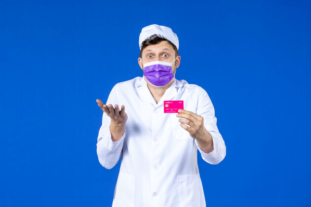男医生前视图中的男医生穿着医疗服和面具持有信用卡的蓝色信用医学病毒