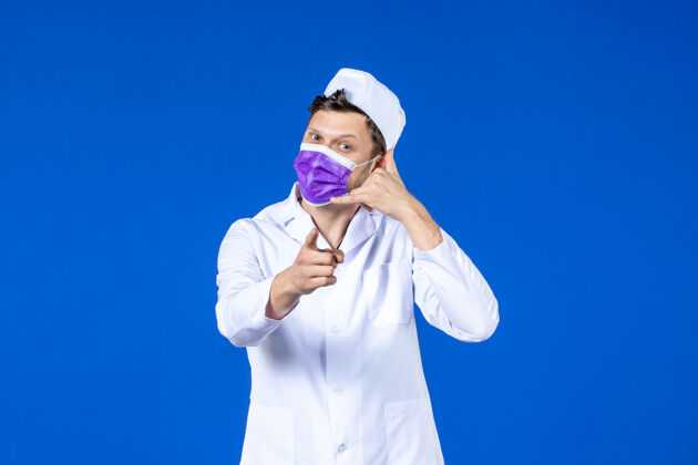 医院身穿医疗服 戴着紫色口罩的男医生在蓝色屏幕上模拟打电话疾病模仿大流行