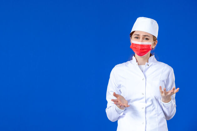 西装压力重重的年轻护士的正视图 身着医疗服 蓝色面罩上戴着红色面罩医药病毒帽子